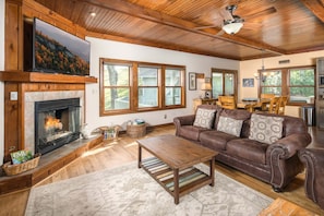 A living room with a fireplace, leather sofa, wooden coffee table, and large windows.