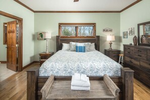 A bedroom with a large bed, wooden headboard, bedside tables, a dresser, and a window with a view.