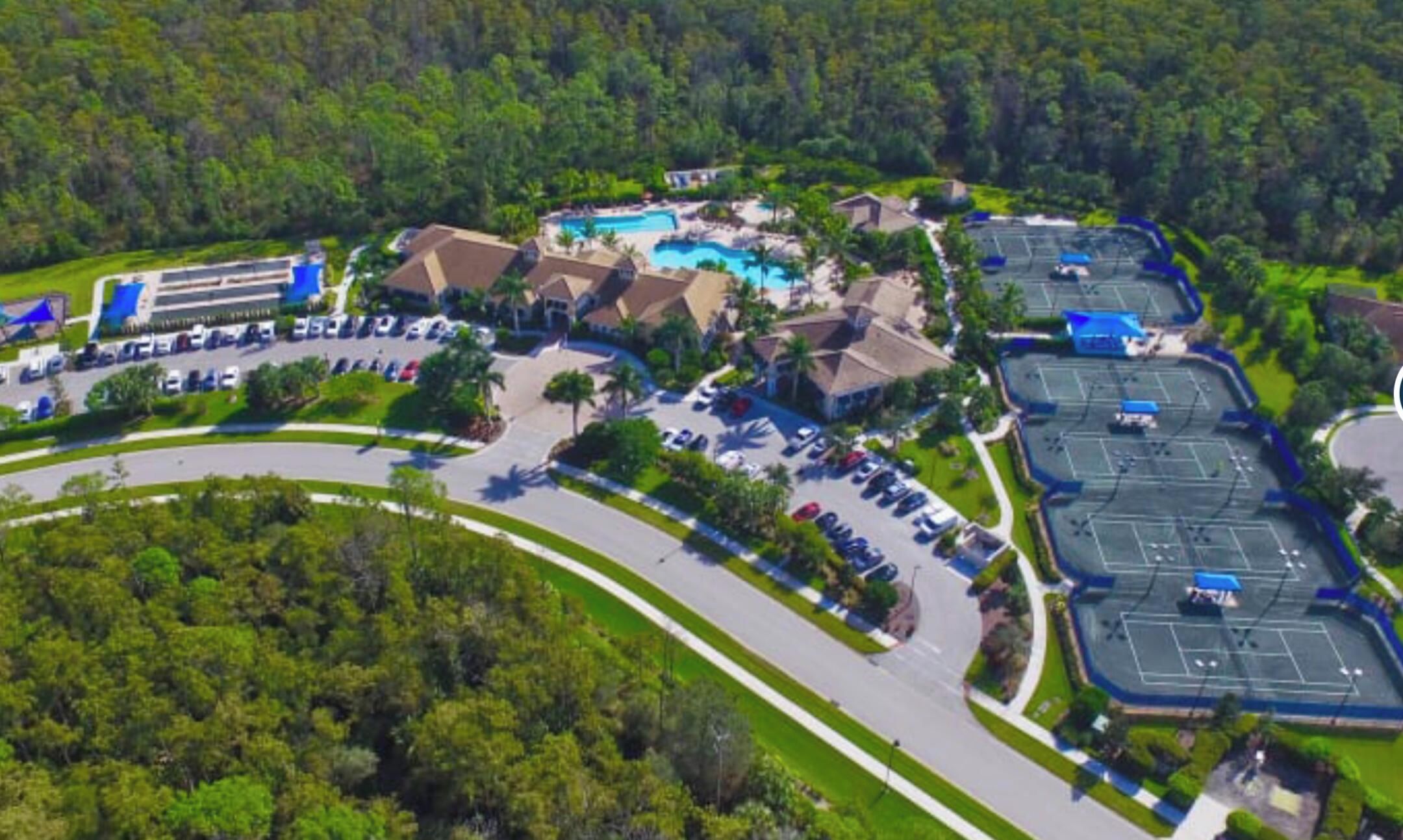 An aerial view of a resort with multiple buildings, a swimming pool, and a parking area surrounded by greenery.