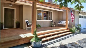 Una terraza de madera con una pérgola, una silla blanca, un farol colgante y una bandera estadounidense.
