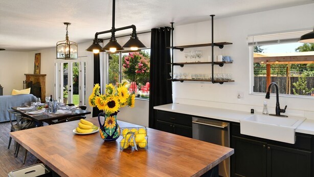 Una cocina moderna con una isla de madera, armarios negros y una ventana con vistas a un jardín.