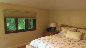 Une chambre à coucher avec un lit, une table de chevet, une lampe et une fenêtre avec des stores.
