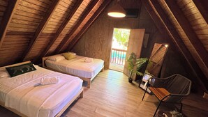 A cozy attic bedroom with two beds, wooden beams, a hanging light fixture, and a view of the outdoors. - Hunter's Cabin PR (Cabo Rojo)