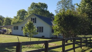 A single-story white house with a blue roof, surrounded by a wooden fence and trees. -  A cozy cottage located 4 miles from Leiper's Fork in Williamson County TN (Thompson's Station)