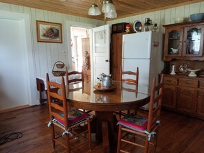 Una mesa de madera con sillas, un refrigerador y un mueble con puertas de vidrio.