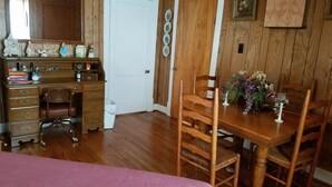 A room with a wooden desk, a chair, a dining table with chairs, a bed with a pink bedspread, and a white door. -  A cozy cottage located 4 miles from Leiper's Fork in Williamson County TN (Thompson's Station)