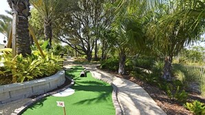 A miniature golf course with a green putting area, numbered hole 14, surrounded by trees and shrubs. - Festive Family Fun! Resort Close 2 Disney! Private Pool! 422 (Davenport)