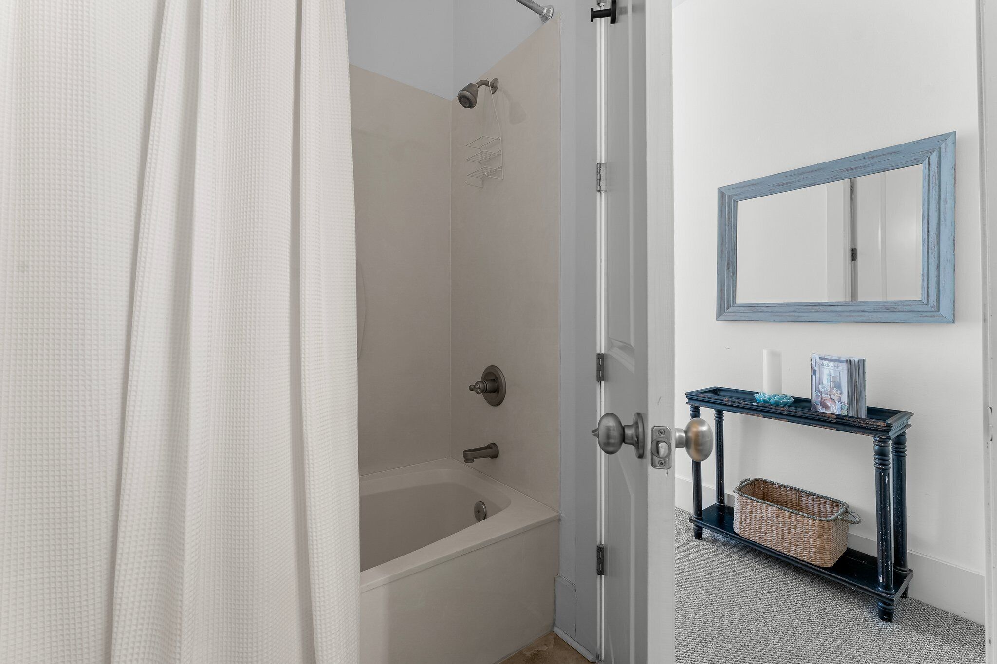 Une salle de bain équipée d’une baignoire, d’une douche, d’un miroir et d’une console sur laquelle est posé un panier.