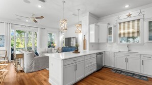 A modern kitchen with white cabinetry, wooden flooring, and pendant lighting.