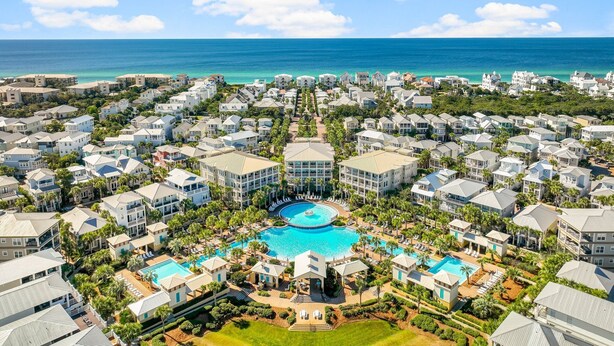A resort with multiple buildings, a central swimming pool, and a view of the ocean.