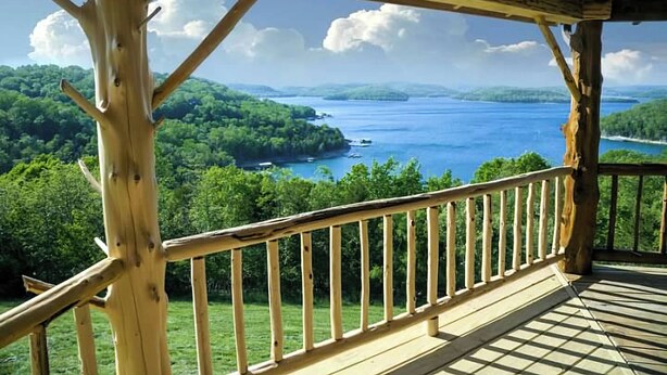 A wooden deck with a railing overlooking a lake surrounded by greenery.
