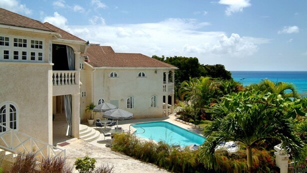 Une grande maison avec une piscine, un patio couvert et une vue sur l’océan.
