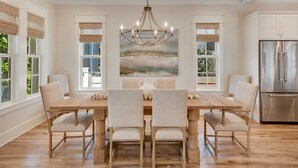 A dining room with a wooden table and chairs, a chandelier, and a large painting on the wall. - PRIVATE BEACH/ POOL ACCESS- Meticulously Maintained- 4 Bikes Included (Rosemary Beach)
