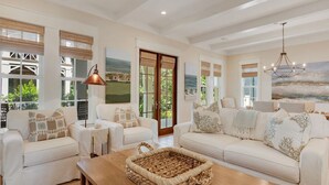 A spacious living room with a large sofa set, a coffee table, and a view of the outdoors through large windows. - PRIVATE BEACH/ POOL ACCESS- Meticulously Maintained- 4 Bikes Included (Rosemary Beach)