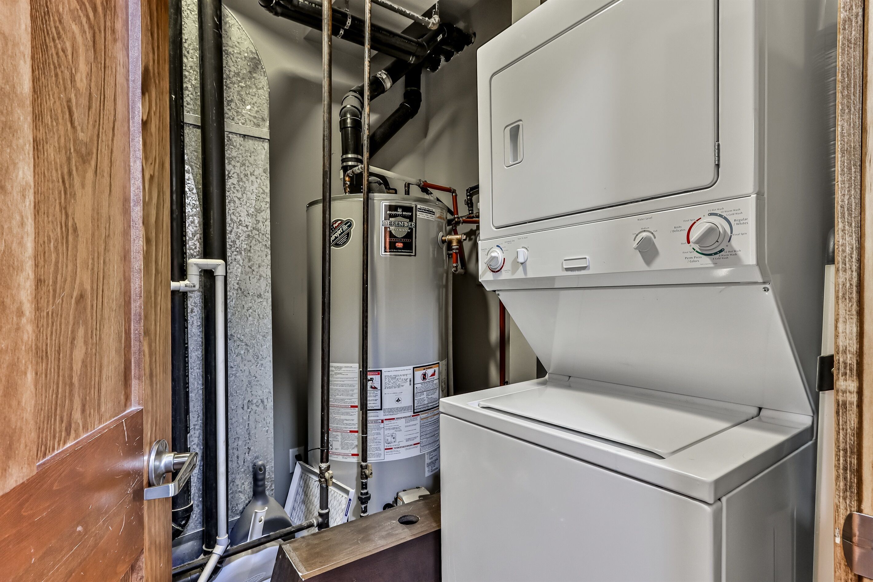 A compact, industrial-style laundry room with a large, white, front-loading washing machine and a water heater.