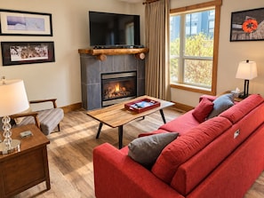 A cozy living room with a fireplace, a red sofa, a wooden coffee table, and framed pictures on the wall. - Spacious, Pet Friendly, Townhouse – Hot Tub | Perfect for Families! (Canmore)