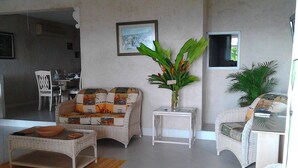 Ein Wohnzimmer mit Sofa, einem Beistelltisch mit Pflanze, einem Essbereich mit Stühlen und einer Küchenzeile.