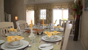 Ein Esszimmer mit gedecktem Tisch, Stühlen, einem Deckenventilator und einem Fenster mit Vorhängen.