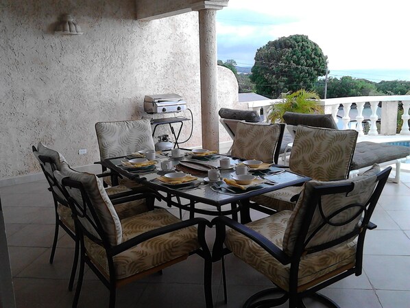 A dining area with a table set for four, surrounded by chairs with patterned cushions. A gas stove is visible in the background. - 3 Bedroom Barbados beach villa-Ocean Views! Private pool, Wifi, A/C, Relaxation (Fryers Well)