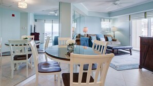 A spacious dining area with a round table and white chairs, a living room with a sofa and armchairs, and a large mirror reflecting the room. - Golf Cart ~ Spacious Living Area ~ Private Balcony (Miramar Beach)