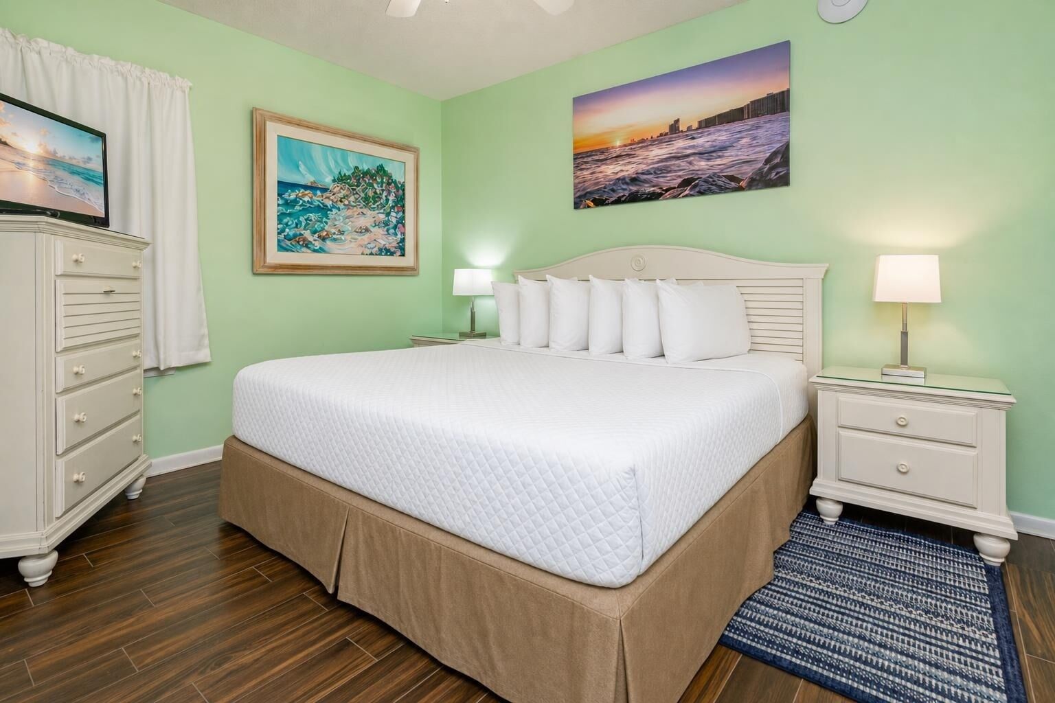 Een keurig opgemaakt slaapkamer met een bed, nachtkastjes, een dressoir en kunstwerken aan de muur.