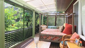 Habitación con cama, una mesita y una silla. Se ve follaje verde a través de la ventana.