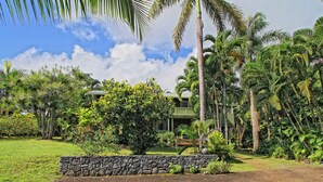 Un resort tropical con un muro de piedra, exuberante follaje y un edificio de dos pisos con balcón.