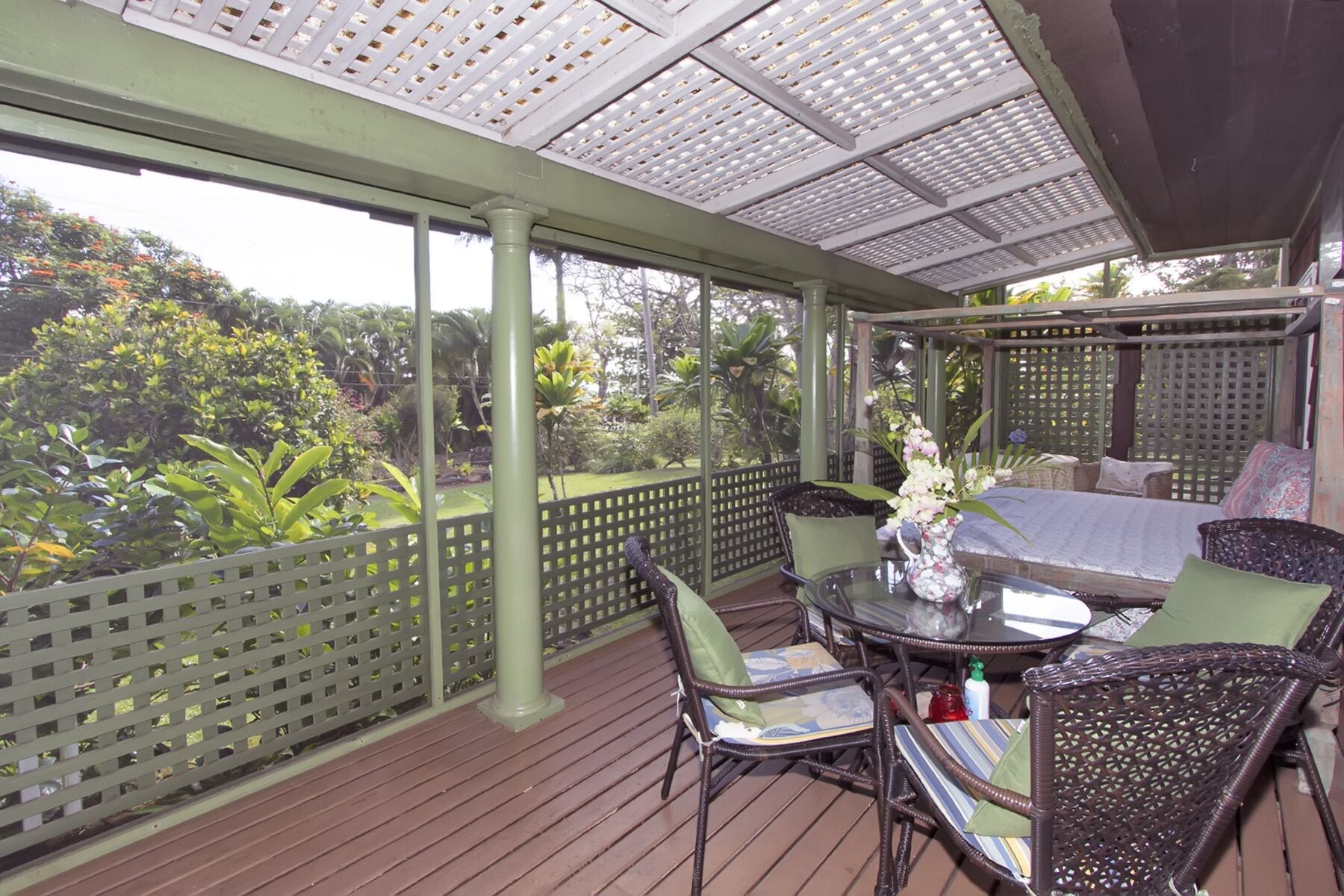 A covered outdoor seating area with a table and chairs, surrounded by a wooden deck and a lattice fence.