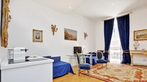 A modern living room with a glass coffee table, blue sofas, a red patterned rug, and a large window with blue curtains. - Amazing Suite Piazza Venezia Suite Int. 3 (Roma)