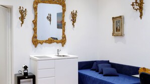 A room with a white cabinet, a blue sofa, a gold-framed mirror, and wall-mounted sconces. - Amazing Suite Piazza Venezia Suite Int. 3 (Roma)