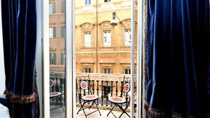 A balcony with two chairs and a table, overlooking a street with buildings. - Amazing Suite Piazza Venezia Suite Int. 3 (Roma)
