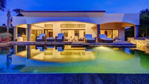 Ein modernes Haus mit Swimmingpool, Sitzgelegenheiten im Freien und einem gut beleuchteten Eingang.