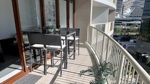 A balcony with wicker furniture, a glass table, and a potted plant.