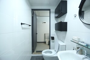 A modern bathroom with a toilet, sink, and mirror. There is a towel rack and a trash bin.