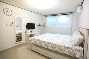 A bedroom with a bed, a wall clock, a TV, a window, and a bedside table.