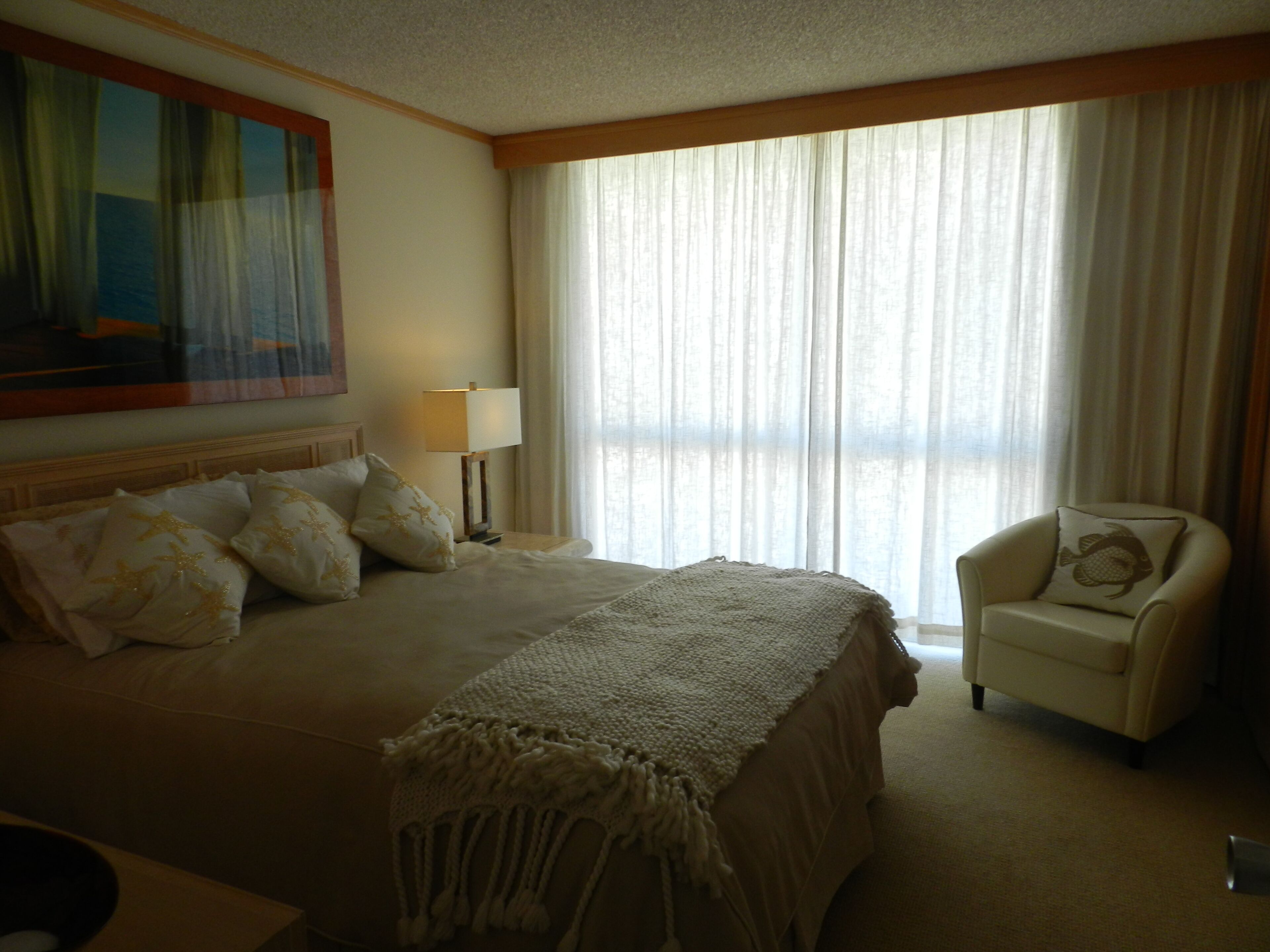 Una habitación de hotel con una cama grande, una silla, una lámpara y un cuadro en la pared.