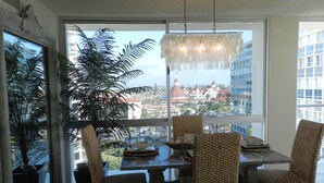A dining area with wicker chairs, a table, and a view of a cityscape through large windows. - Corondo Shores Unique  & Beautiful Condo -  Stunning Views!!!  Pet Welcome! (Coronado)