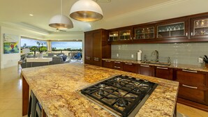 A modern kitchen with granite countertops, a gas stove, wooden cabinets, and pendant lighting. - Spectacular 3rd Row Villa at Ho'olei with Ocean Views (Kihei)