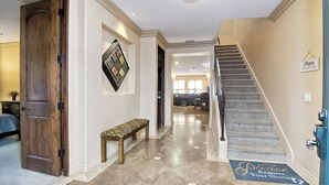 A hallway with a wooden bench, a staircase, and a mat at the bottom of the stairs with a shoe-removal request.