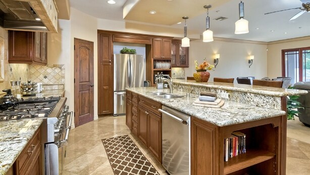 A modern kitchen with granite countertops, stainless steel appliances, wooden cabinets, and pendant lighting.