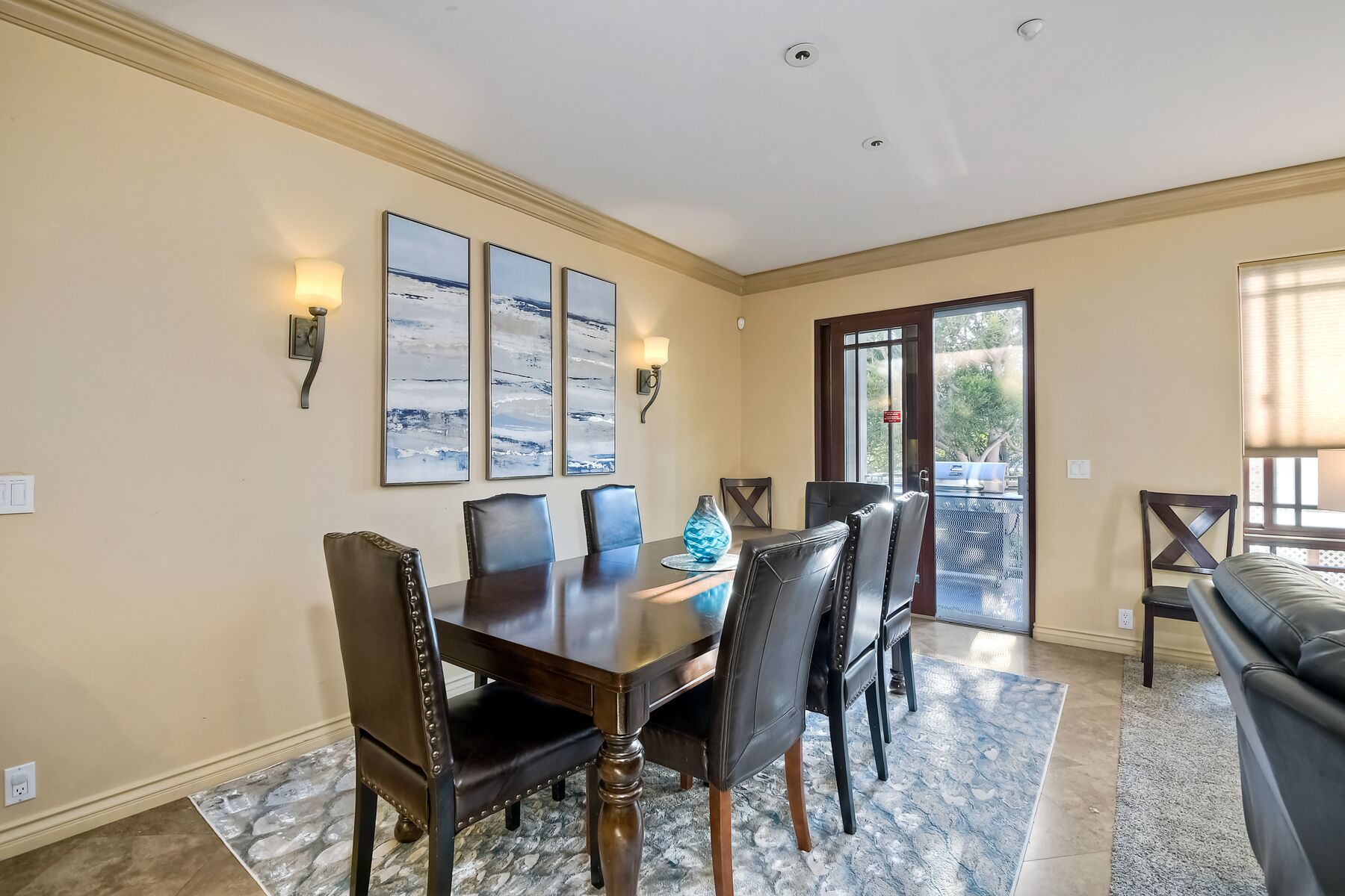 A dining area with a wooden table and six chairs, a rug, and three abstract paintings on the wall.