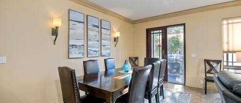 A dining area with a wooden table and six chairs, a rug, and three abstract paintings on the wall.