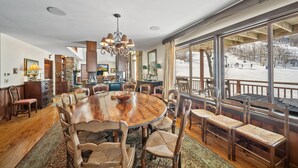 Un vaste espace dédié à la salle à manger, avec une grande table et des chaises en bois, le tout entouré de grandes fenêtres offrant une vue sur un paysage enneigé.