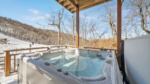 Un bain à remous sous une pergola en bois, avec un paysage enneigé en arrière-plan.
