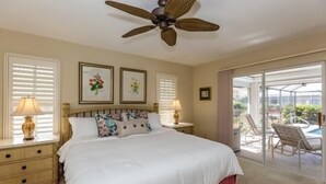A bedroom with a bed, two bedside tables, a ceiling fan, and a view of an outdoor pool area. - Waterfront home on the famous Paradise Coast (Marco Island)