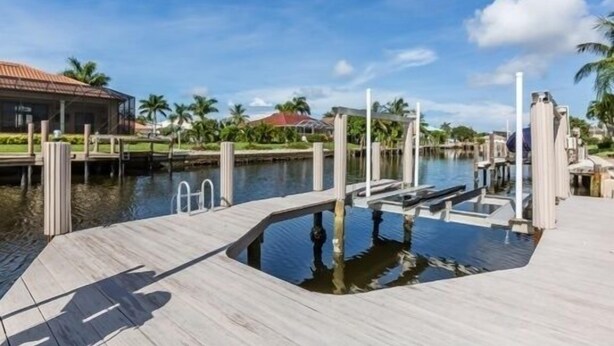 A waterfront dock with a pool, palm trees, and a building with a red roof in the background. - Waterfront home on the famous Paradise Coast (Marco Island)