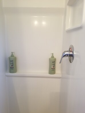 Ein Badezimmer mit einer weißen Badewanne, zwei Flaschen Suave Duschgel auf einem Regal und einem Chrom-Wasserhahn.