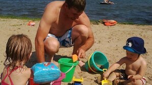 A beach scene with a man and two children playing with sand toys. - Gun Lake Cottage shared lake frontage, 7 Miles to Casino, Volleyball Playgrounds (Wayland)