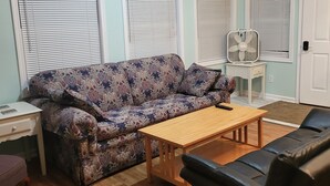 A living room with a sofa, a wooden table, a black leather couch, and a fan on a small table. - Gun Lake Cottage shared lake frontage, 7 Miles to Casino, Volleyball Playgrounds (Wayland)
