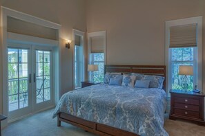 Une chambre avec un grand lit, deux tables de chevet et une vue à travers les portes vitrées.
